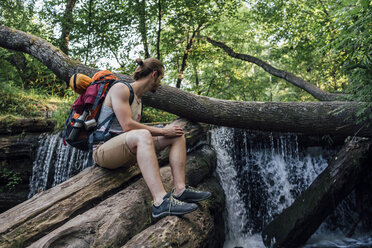 Junger Mann mit Rucksack bei einer Pause in einem Wald in der Nähe eines Wasserfalls - VPIF01166