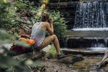 Rückansicht eines Wanderers im Wald, der einen Wasserfall fotografiert - VPIF01169
