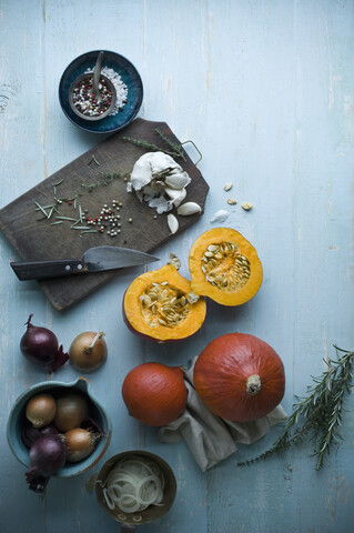 Geschnittener und ganzer Hokkaidokürbis, Zwiebeln, Knoblauch und Kräuter auf Holz, lizenzfreies Stockfoto