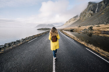 Island, Rückenansicht einer Frau mit Rucksack, die auf dem Mittelstreifen einer Landstraße geht - OCMF00120