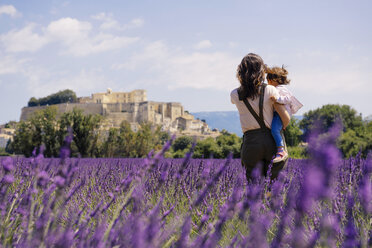 France, Grignan, back view of mother standing in lavender field with little daughter on her arms - GEMF02590