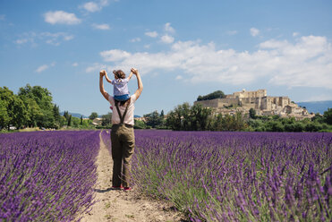 France, Grignan, back view of mother standing between lavender fields with little daughter on her shoulders - GEMF02603