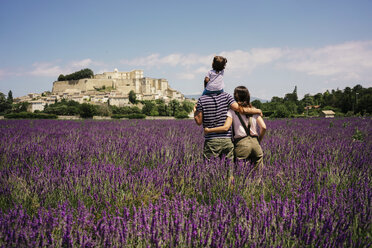 Frankreich, Grignan, Rückenansicht einer Familie im Lavendelfeld mit Blick auf das Dorf - GEMF02606
