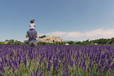 France, Grignan, back view of father standing in lavender field with little daughter on his shoulders - GEMF02612