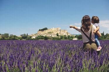 France, Grignan, back view of mother and little daughter standing together in lavender field looking at village - GEMF02621