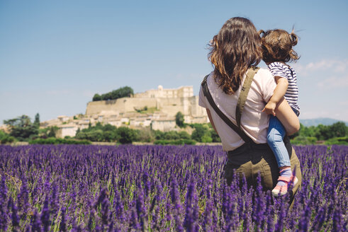 France, Grignan, back view of mother and little daughter together in lavender field looking at village - GEMF02623