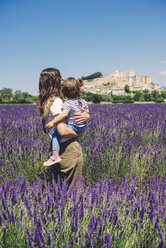 France, Grignan, back view of mother and little daughter standing together in lavender field looking at village - GEMF02625