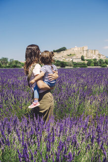 Frankreich, Grignan, Rückenansicht von Mutter und kleiner Tochter, die zusammen in einem Lavendelfeld stehen und auf das Dorf blicken - GEMF02625