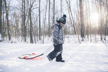 Seitenansicht eines Jungen mit Schlitten auf einem verschneiten Feld vor kahlen Bäumen - CAVF56772