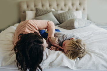 Happy mother playing with son while lying on bed at home - CAVF56779