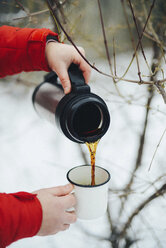 Abgeschnittene Hände einer Frau, die im Winter schwarzen Kaffee aus einem isolierten Getränkebehälter in einen Becher gießt - CAVF56791