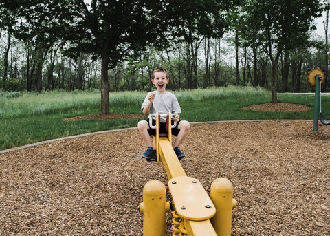 Porträt eines glücklichen Jungen, der im Park auf einer Wippe spielt, lizenzfreies Stockfoto