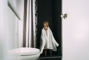 Boy wrapped in towel standing by bathroom doorway at home - CAVF56816