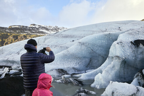 Rückansicht eines Vaters mit Tochter, der Gletscher fotografiert, während er gegen den Himmel steht - CAVF56833