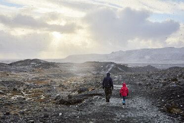 Rear view of father with daughter walking on mountain against cloudy sky during sunset - CAVF56835