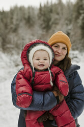 Portrait of mother carrying daughter while standing in forest during winter - CAVF56850