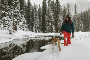 Frau mit Hund auf schneebedecktem Feld im Wald spazierend - CAVF56856