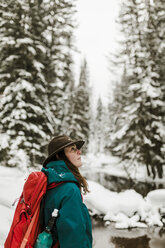 Side view of woman with backpack standing in snow covered forest - CAVF56858