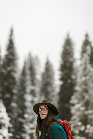 Seitenansicht einer Frau mit Rucksack vor dem Himmel in einem verschneiten Wald, lizenzfreies Stockfoto