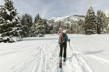 Rear view of woman with skies walking on snow covered field against sky - CAVF56863