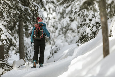 Rear view of woman with skies standing on snow covered field at forest - CAVF56864