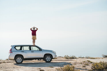 Rear view of man standing on car roof against sea and sky - CAVF56932