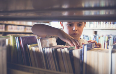 Ernster Junge auf der Suche nach einem Buch aus dem Regal in der Bibliothek - CAVF56937