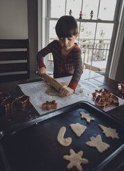 Junge rollt Plätzchenteig auf dem Tisch während Weihnachten zu Hause - CAVF56939