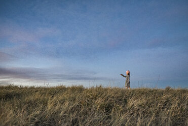 Side view of girl standing on grassy field against sky during sunset - CAVF56992