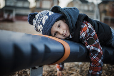 Portrait of cute boy lying on outdoor play equipment at playground - CAVF57029