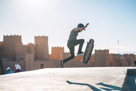 Seitenansicht eines Mannes, der einen Stunt auf einem Skateboard gegen ein Schloss bei sonnigem Wetter vollführt, lizenzfreies Stockfoto