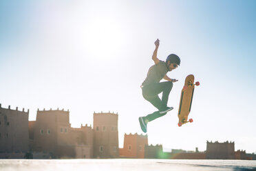 Mann führt Stunt auf dem Skateboard gegen eine Burg in voller Länge an einem sonnigen Tag aus - CAVF57059