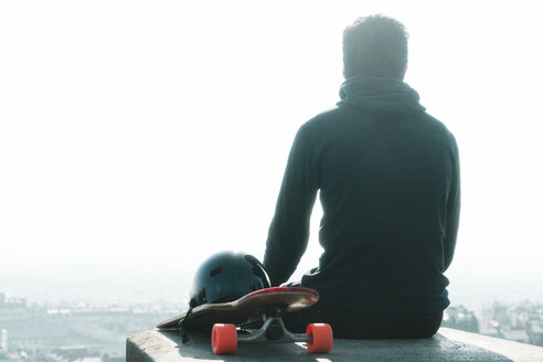 Rückansicht eines auf einer Säule sitzenden Mannes mit Skateboard gegen den klaren Himmel - CAVF57062