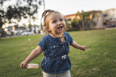 Glückliches Baby-Mädchen, das wegschaut, während es auf einer Wiese gegen den Himmel im Park steht - CAVF57119