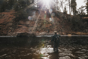 Rückansicht eines männlichen Wanderers mit Rucksack beim Angeln im Fluss am Berg - CAVF57142