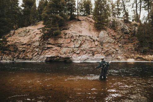 Rückansicht eines männlichen Wanderers mit Rucksack beim Angeln im Fluss am Berg - CAVF57143