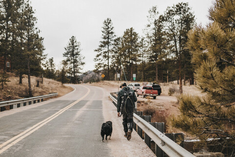 Rückansicht eines männlichen Wanderers mit Hund auf der Straße, lizenzfreies Stockfoto