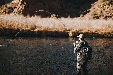 Side view of male hiker with backpack fishing in river at forest - CAVF57149