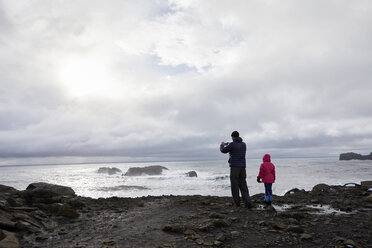 Rückansicht von Vater und Tochter am Strand stehend gegen bewölkten Himmel - CAVF57157