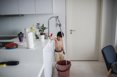 Shirtless boy filling water in bucket at home - CAVF57158