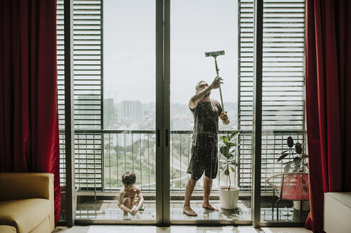 Vater mit Sohn beim Fensterputzen auf dem Balkon durch Glas gesehen - CAVF57161