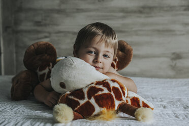 Portrait of boy playing with stuffed toys on bed at home - CAVF57196