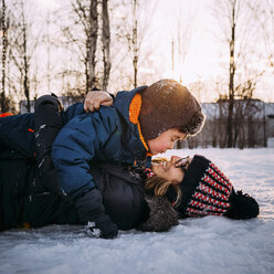 Glückliche Mutter mit Sohn auf schneebedecktem Feld gegen den Himmel bei Sonnenuntergang liegend - CAVF57201