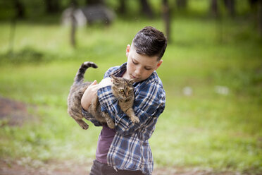 Boy holding cat while standing on field - CAVF57204