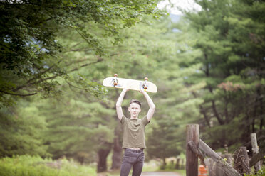 Porträt eines Teenagers, der ein Skateboard hält, während er an einem Baum steht - CAVF57205