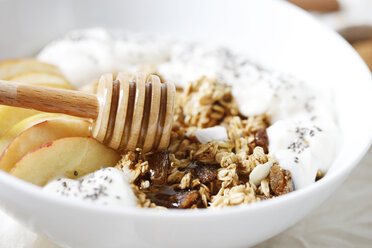 Close-up of honey dipper with sliced apple and yogurt in breakfast cereals on table - CAVF57218