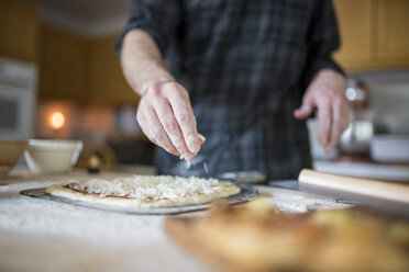 Mittelteil eines Mannes, der in der Küche Zutaten auf eine Pizza streut - CAVF57227