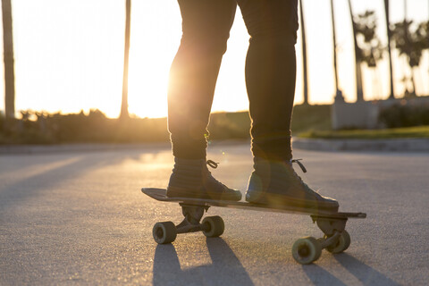 Niedriger Ausschnitt einer Frau, die bei Sonnenuntergang auf einem Skateboard steht, lizenzfreies Stockfoto