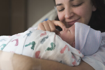 Close-up of mother playing with newborn son while relaxing on bed at hospital - CAVF57276