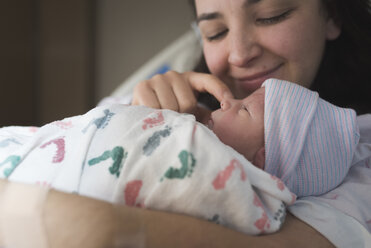 Nahaufnahme einer Mutter, die mit ihrem neugeborenen Sohn spielt, während sie sich auf dem Bett im Krankenhaus ausruht - CAVF57276
